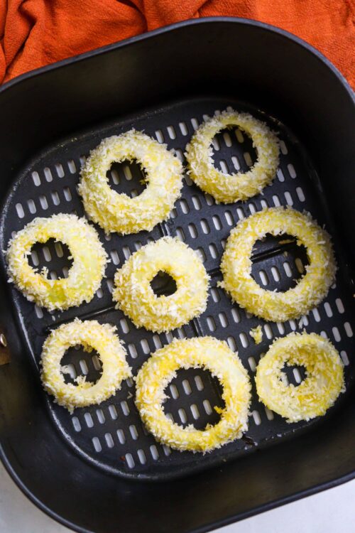 Golden coconut-covered onion rings in an air fryer basket.