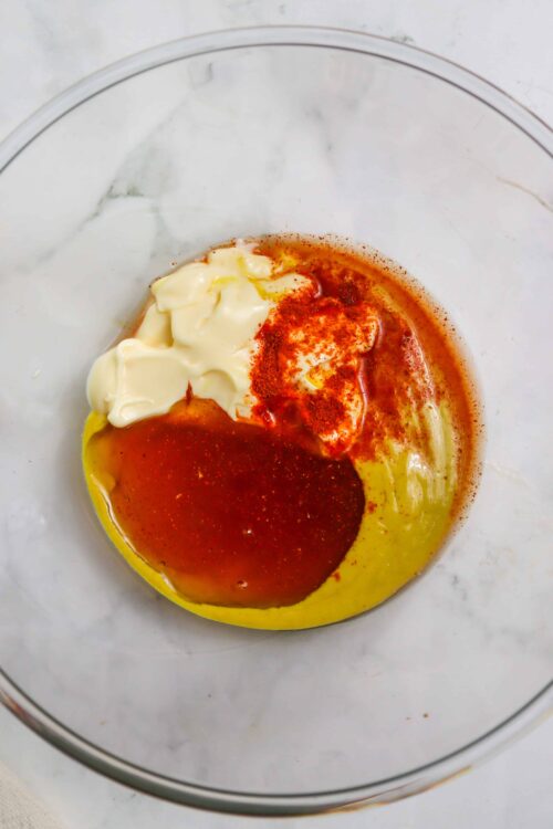 Cream cheese, hot sauce, and spices in a glass bowl for buffalo chicken dip.