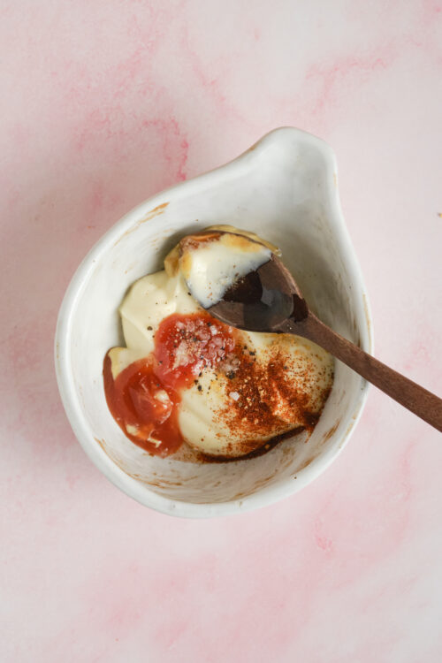 Sweet creamy yogurt with tomato sauce and spices in a white bowl on pink background.