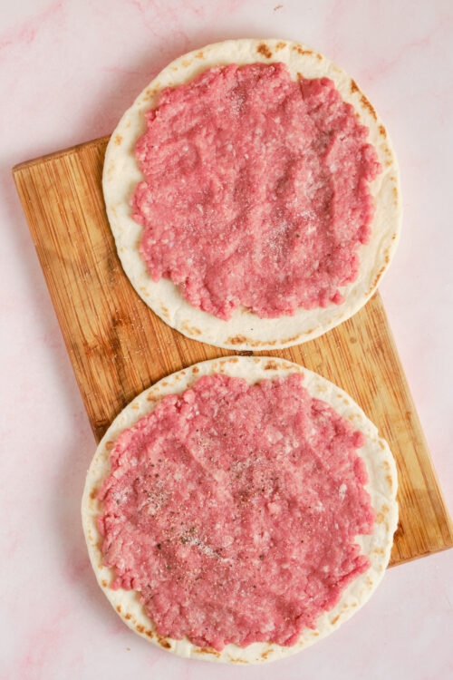 Freshly made pizza with pink sauce on round flatbread, ready to bake.; Pizza bread with pink sauce for homemade pizza baking.