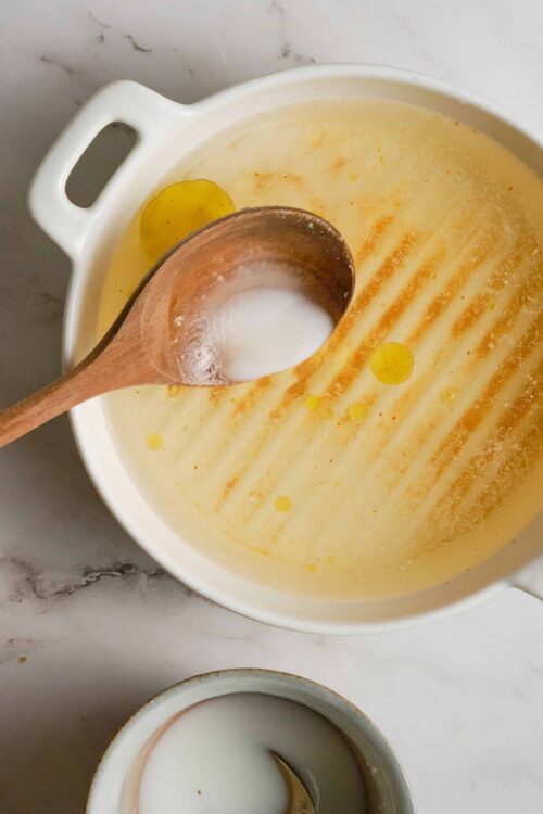 Creamy cheese soup with a wooden spoon in a white bowl.