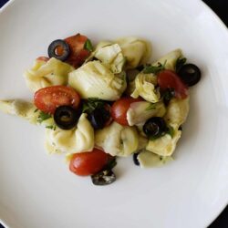 Fresh artichoke heart salad with cherry tomatoes, black olives, and herbs on a white plate.