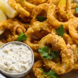 Crispy fried calamari with lemon wedges and creamy dipping sauce, shot on a white plate.