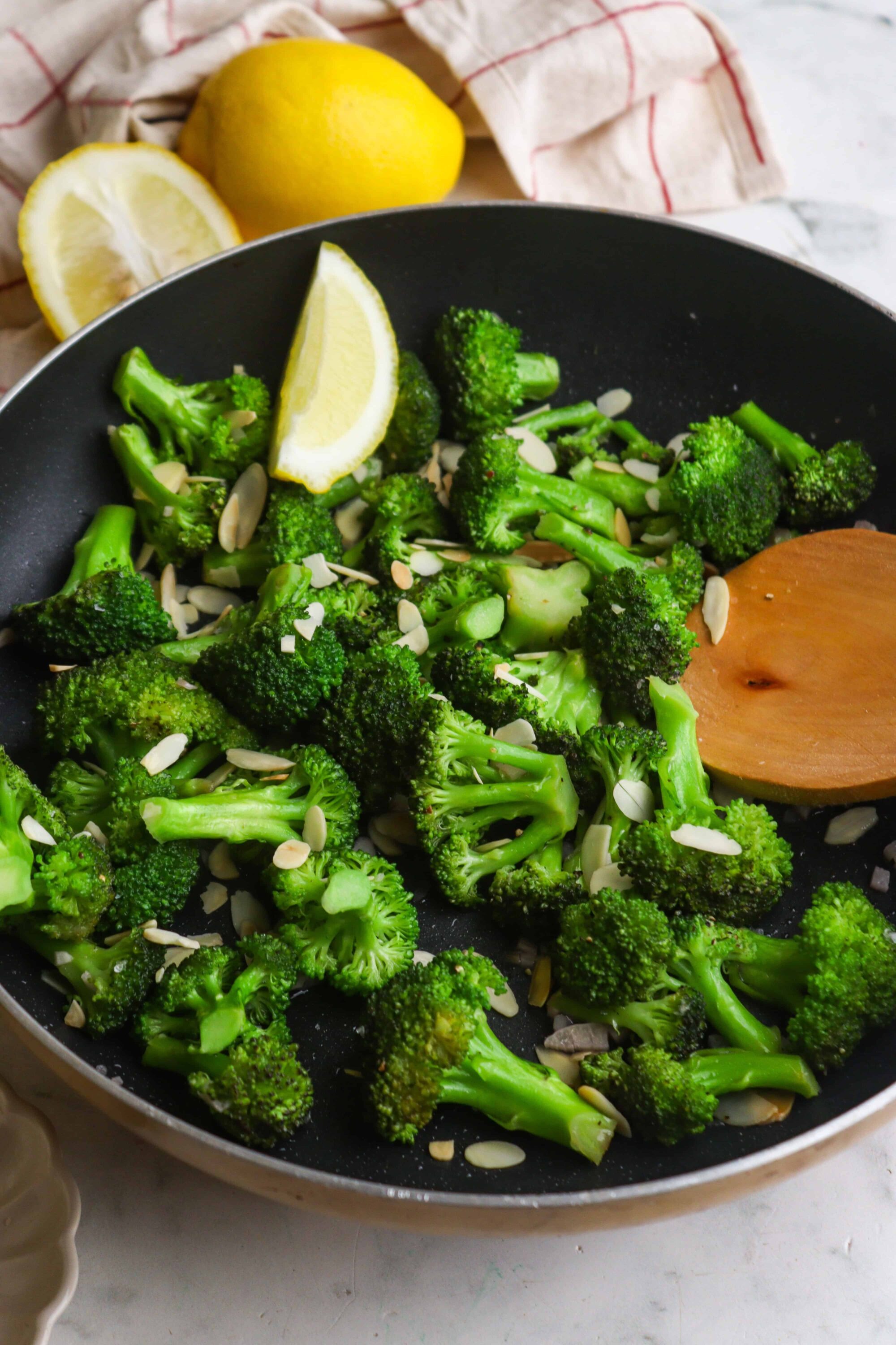 Sautéed broccoli with lemon wedges and sliced almonds in a black skillet.
