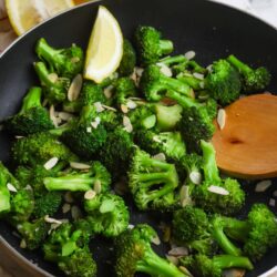 Sautéed broccoli with lemon wedges and sliced almonds in a black skillet.