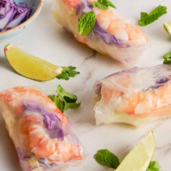 Fresh spring rolls with shrimp and vegetables on a white marble surface, garnished with lime and mint.