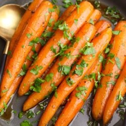 Roasted carrots with fresh parsley and garlic butter in a skillet, healthy vegetable side dish, vibrant orange color.