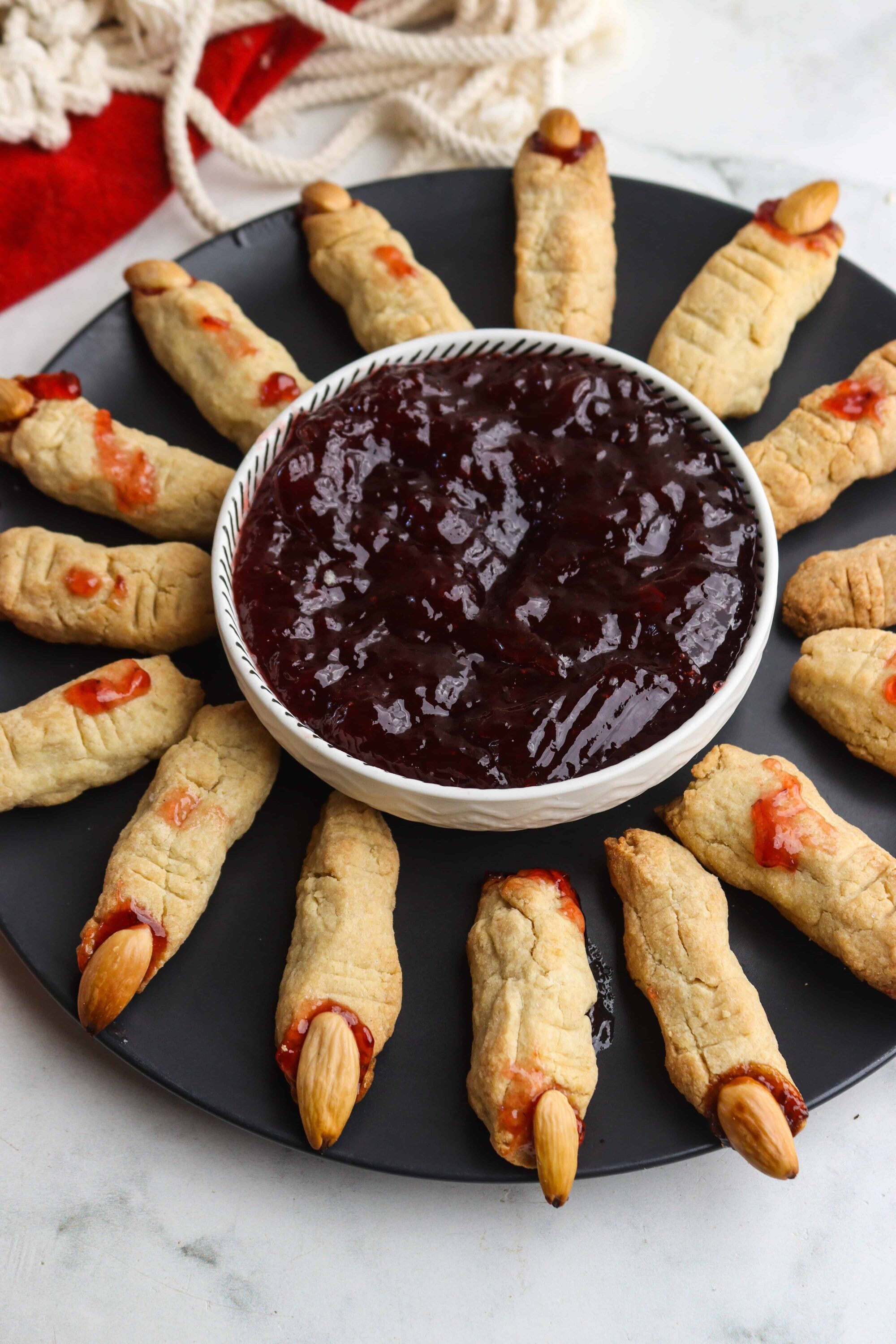 Mini cheese and jam pastry bites with almond topping on a black serving platter.