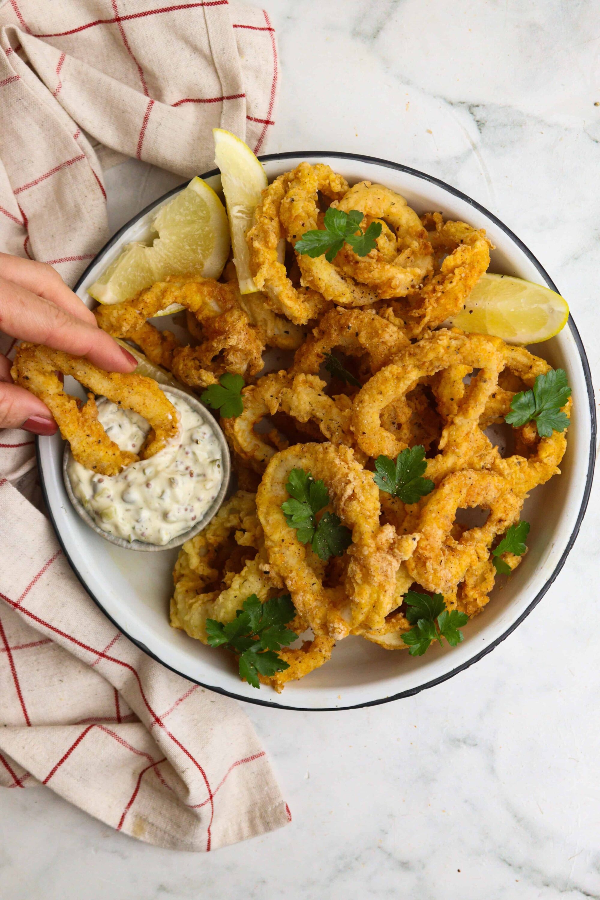 Crispy fried calamari with lemon wedges and tangy aioli dipping sauce on a white platter.