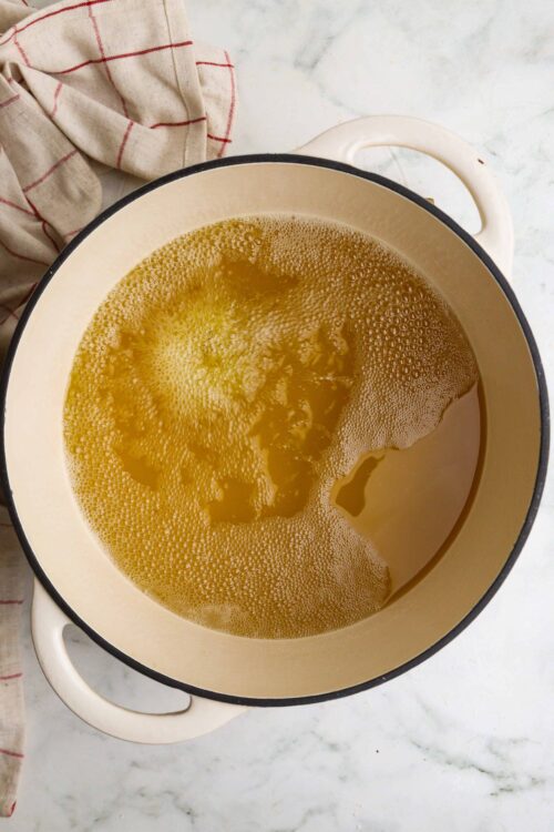 Steaming chicken broth in a cream-colored pot with black trim for savory soup or cooking.
