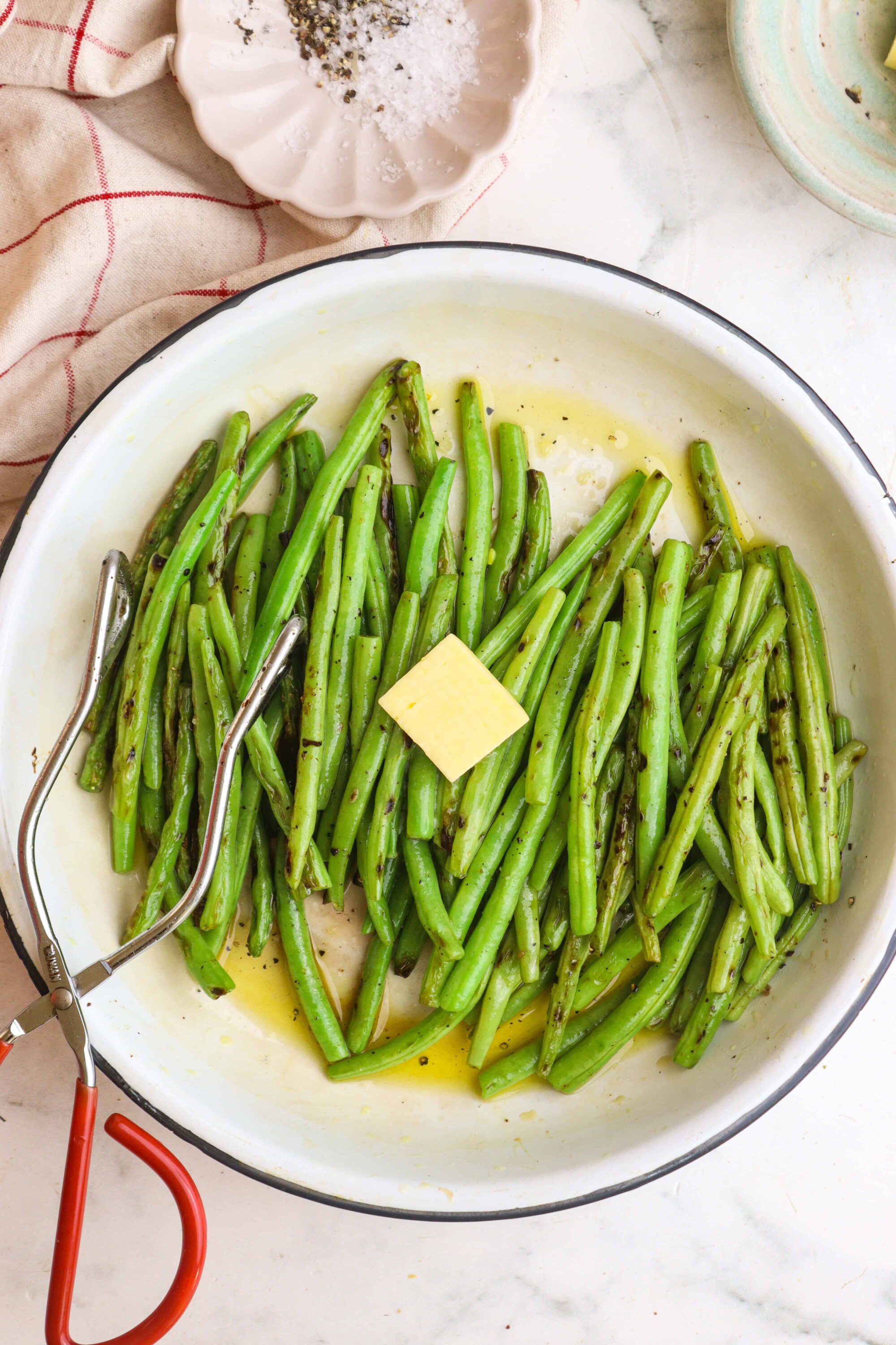 Green beans being prepared with butter and herbs in a white skillet.