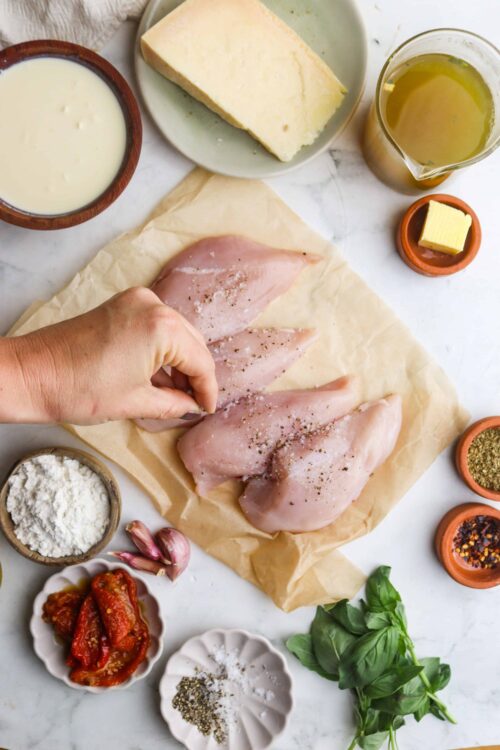 Juicy raw chicken breasts with herbs and spices on parchment paper for baking.