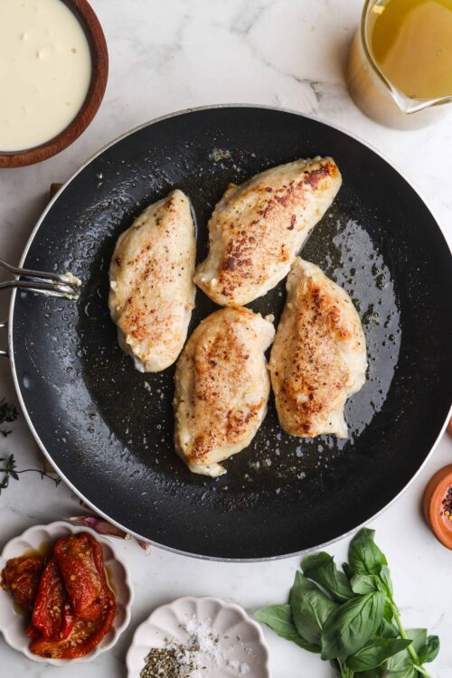 Golden-brown sautéed chicken breasts cooking in a non-stick skillet.