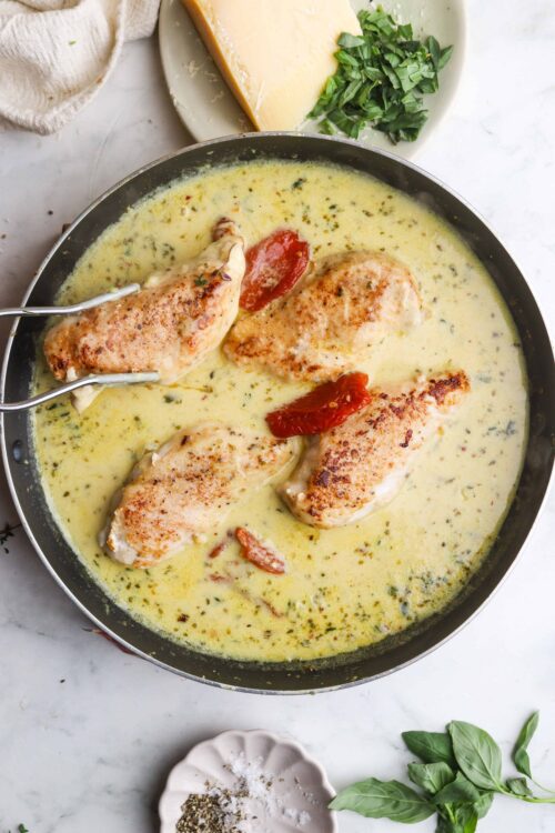Crispy chicken in creamy sauce garnished with sun-dried tomatoes, served in a skillet.