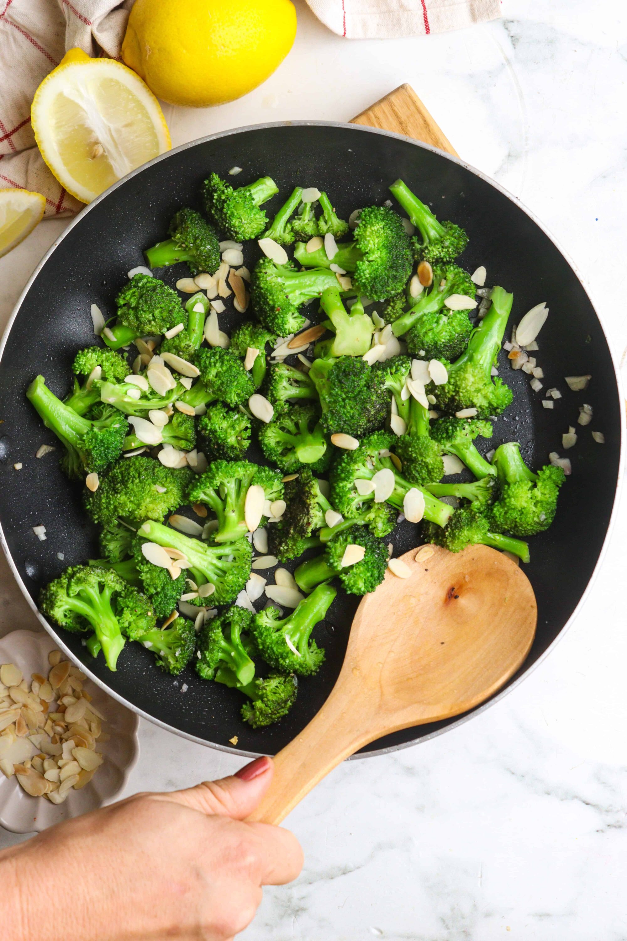 Steamed broccoli with sliced almonds in a black skillet for healthy vegetable dish.