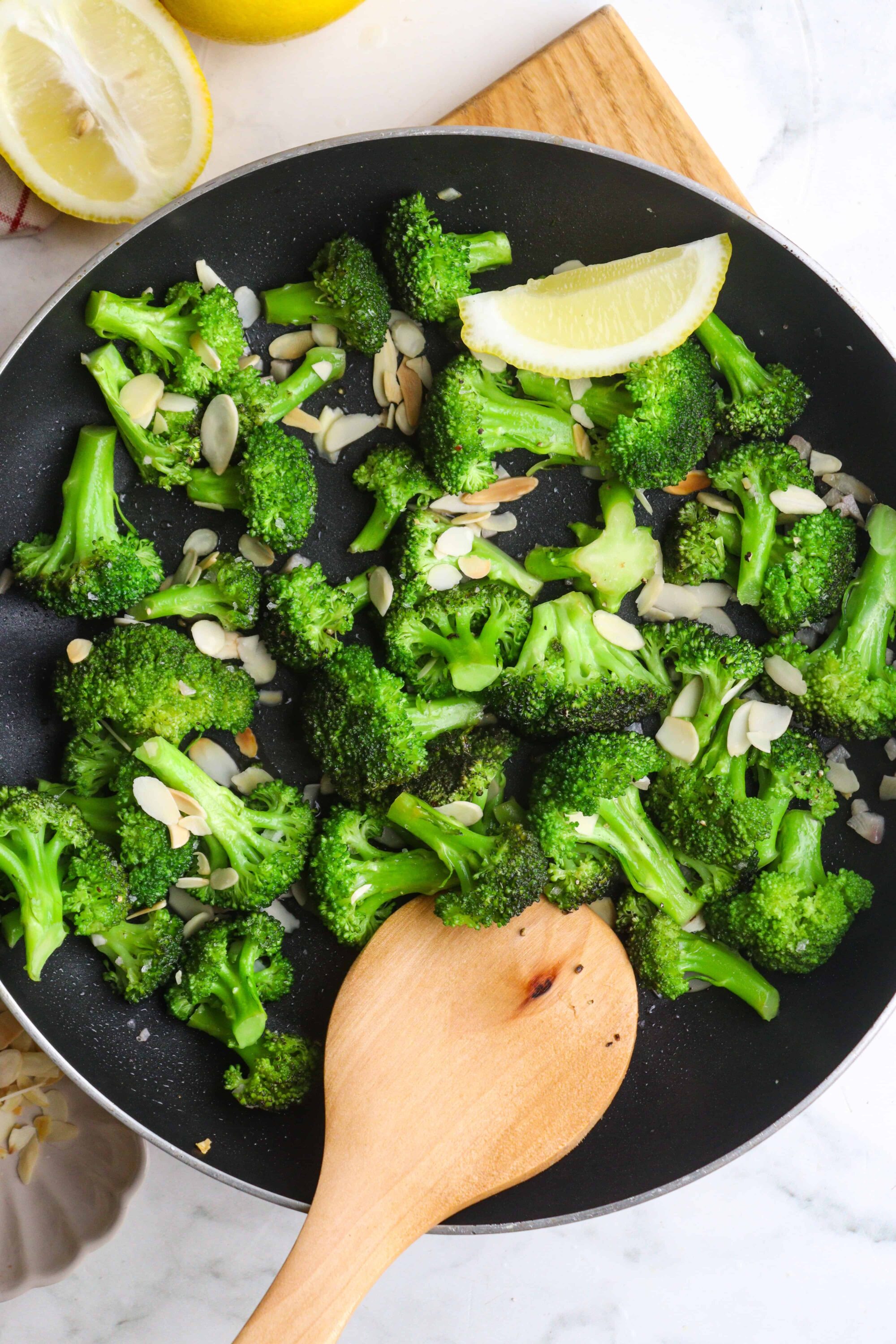 Steamed broccoli with sliced almonds and lemon wedge in a black skillet for healthy side dish.