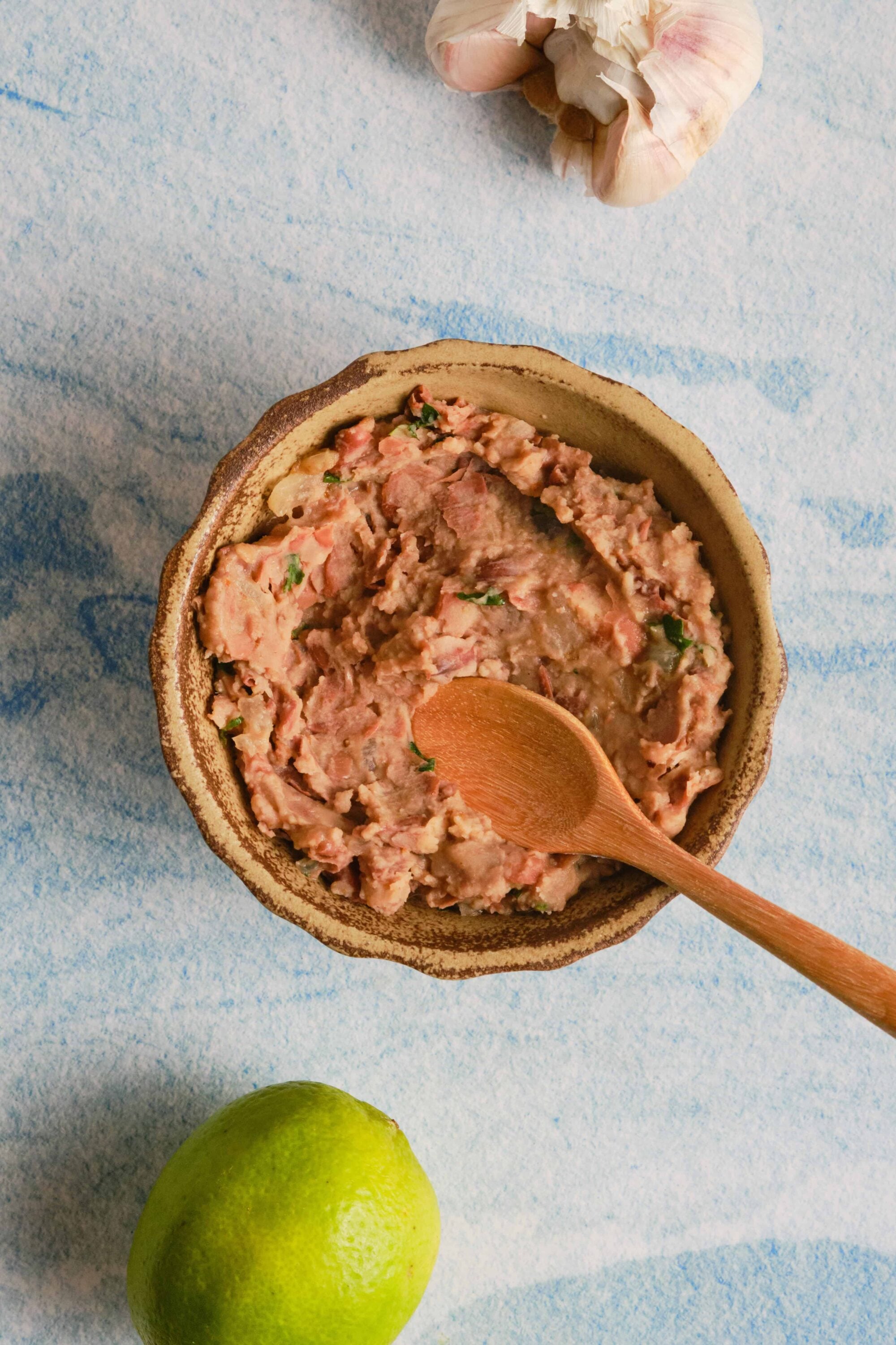 Rustic homemade tuna salad in a ceramic bowl, garnished with herbs on a blue textured background.