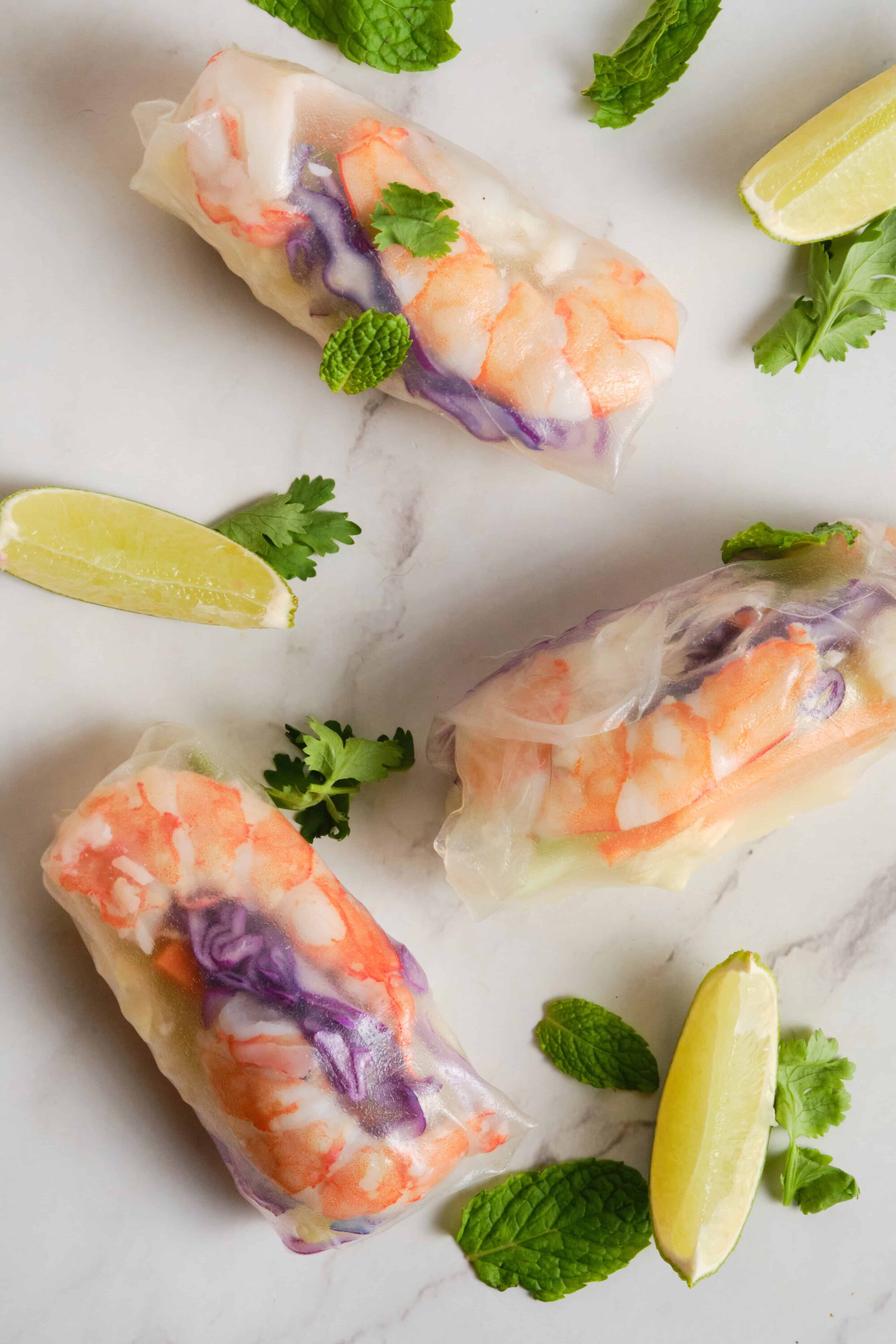 Fresh seafood spring rolls with shrimp, vegetables, and herbs on a marble surface.