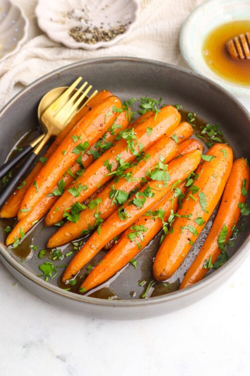 Roasted carrots garnished with fresh herbs on a dark plate.