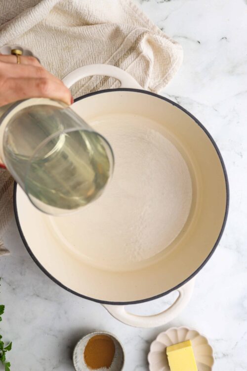 Pouring white wine into a large enameled Dutch oven for cooking.