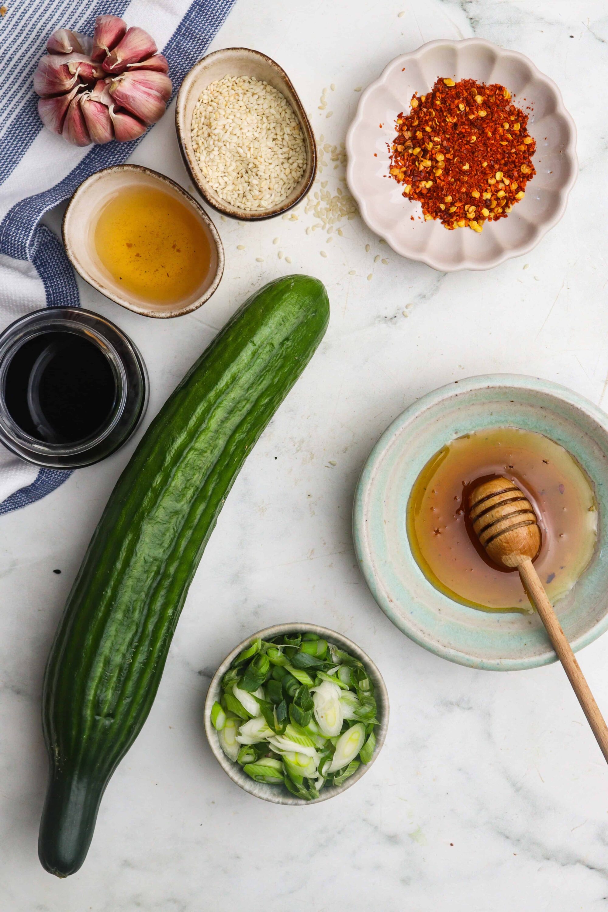 Fresh cucumber and ingredients for Asian-inspired dish with garlic, chili flakes, sesame seeds, and soy sauce.