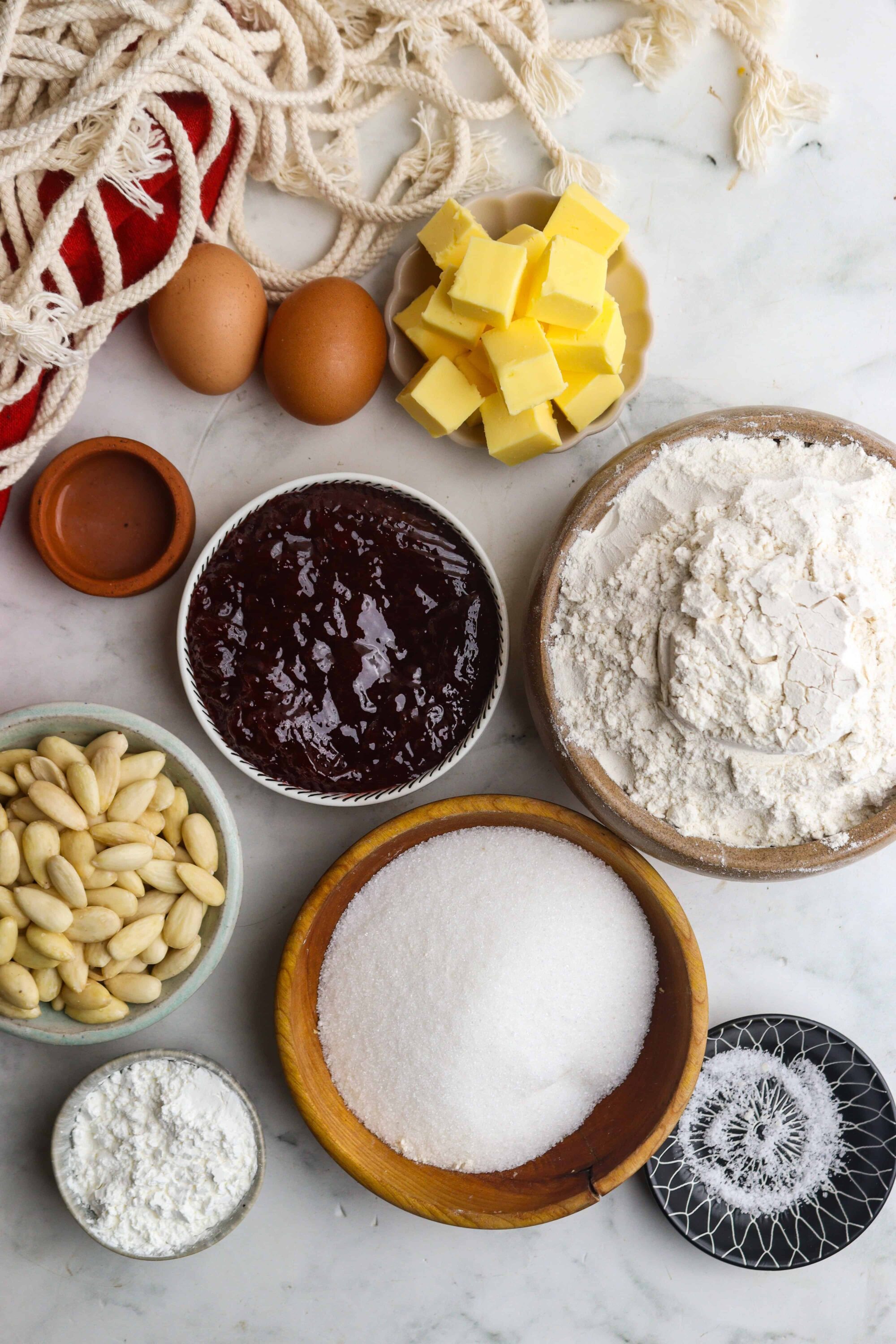 Butter, eggs, chocolate, flour, sugar, vanilla extract, almonds, jam, baking ingredients, baking preparation, dessert ingredients.