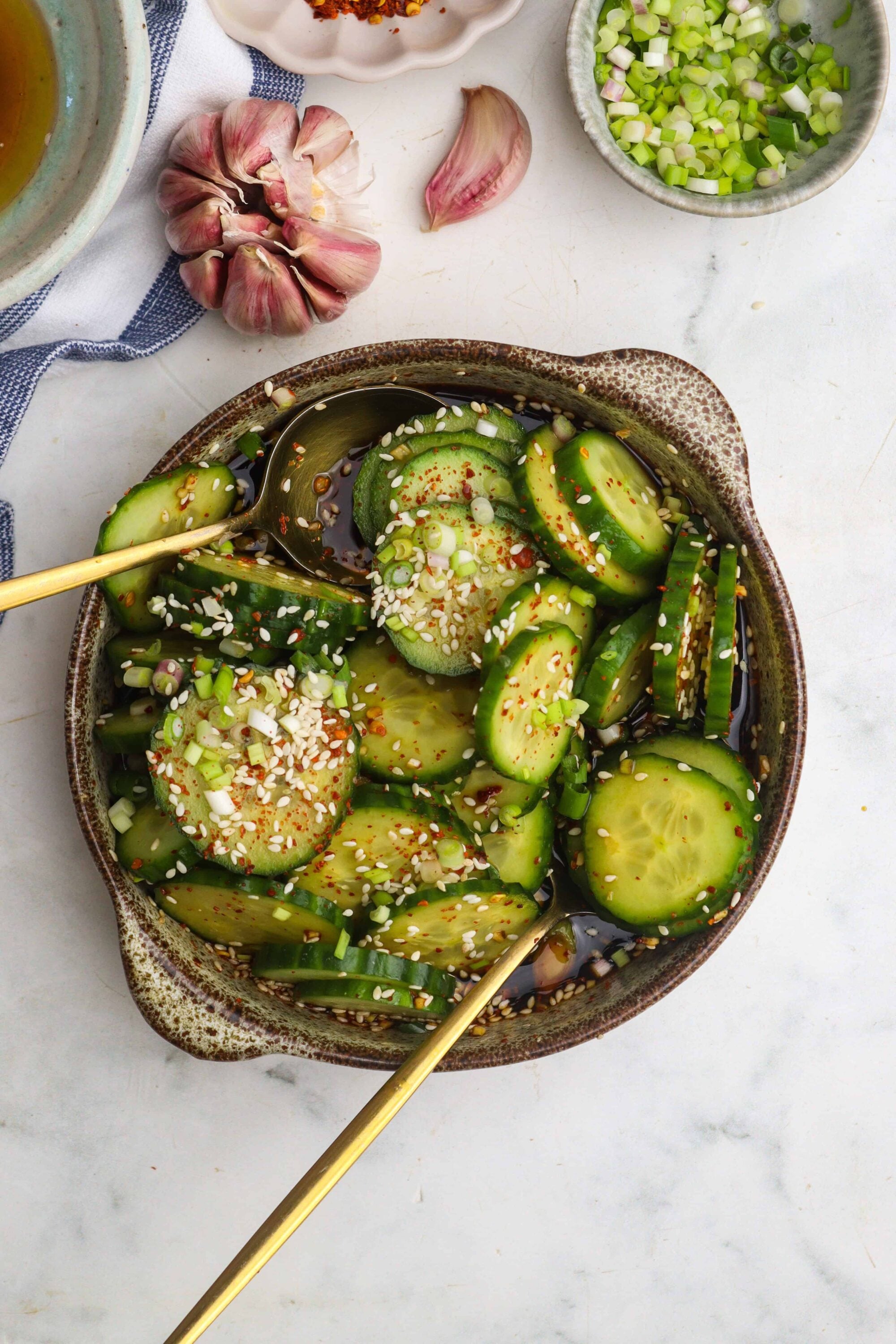 Cucumber salad with sesame seeds, chopped green onions, soy sauce, and chili flakes in a rustic bowl.