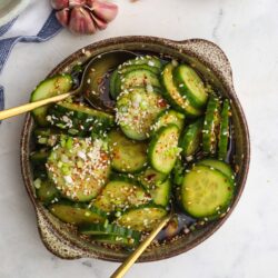 Cucumber salad with sesame seeds, chopped green onions, soy sauce, and chili flakes in a rustic bowl.