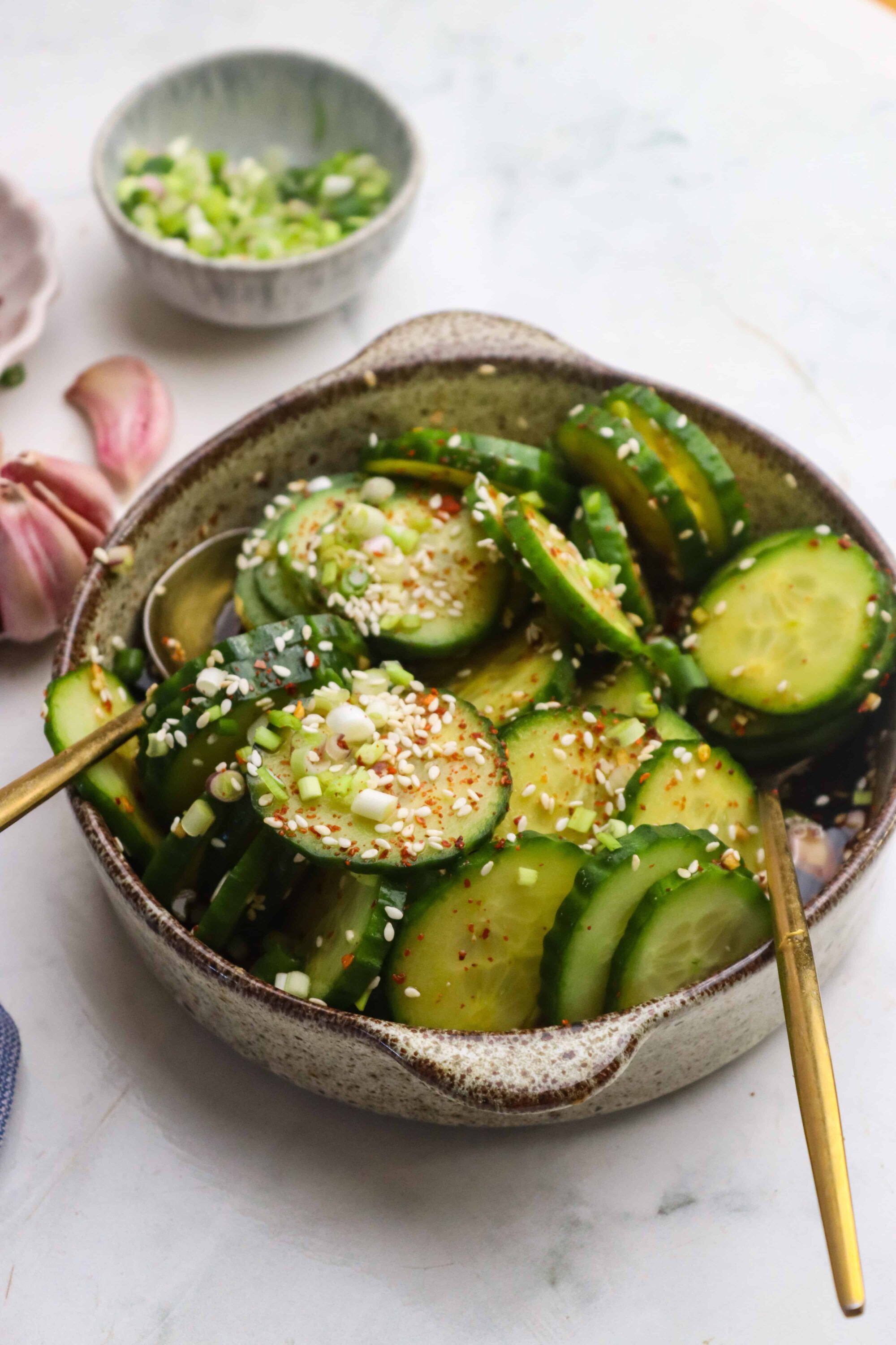 Cucumber salad with sesame seeds and chopped green onions in a rustic bowl, garnished with chili powder for flavor.