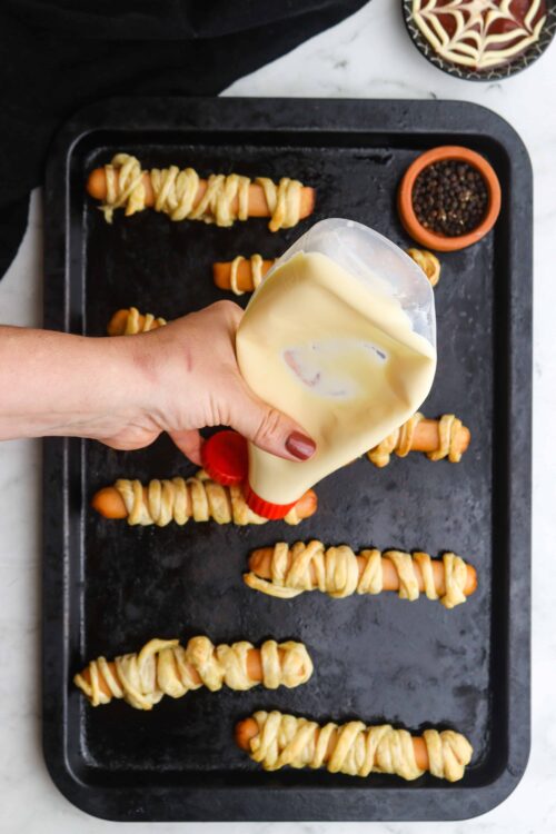 Golden hot dogs wrapped in flaky pastry on a baking sheet.