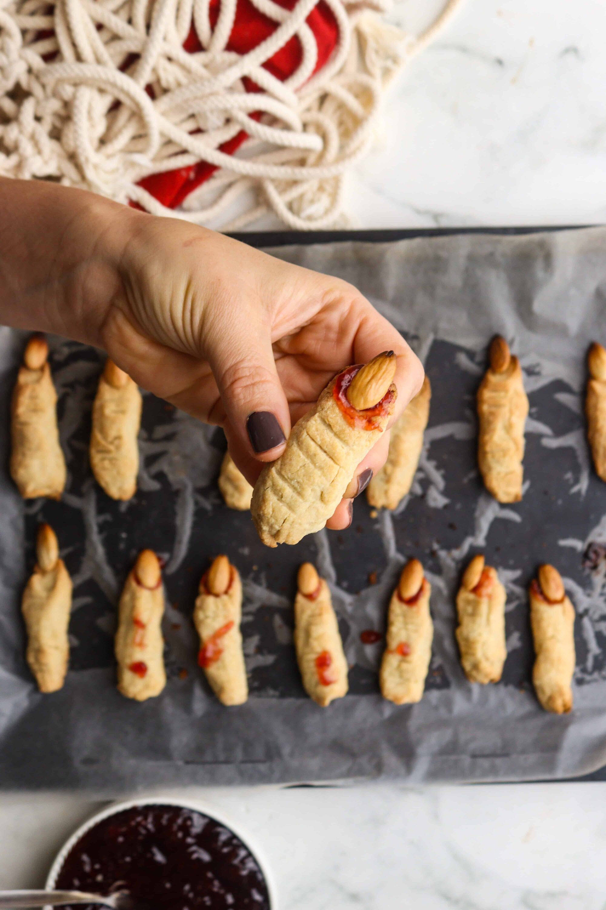 Bite-sized cookies with almonds and red jam on baking sheet.