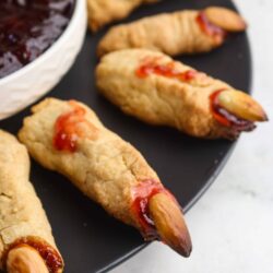 Mini Halloween mummies with almond eyes on black platter, served with berry jam. Delicious, spooky treats for Halloween parties.