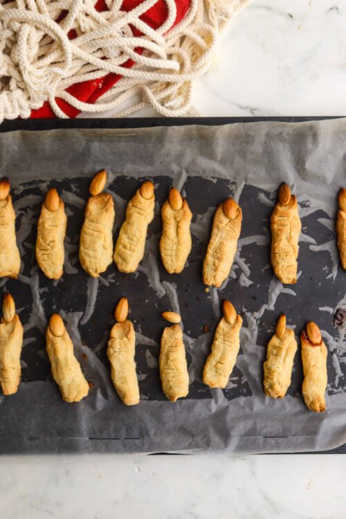 Golden baked cookies shaped like rats with almonds on top on a baking sheet.