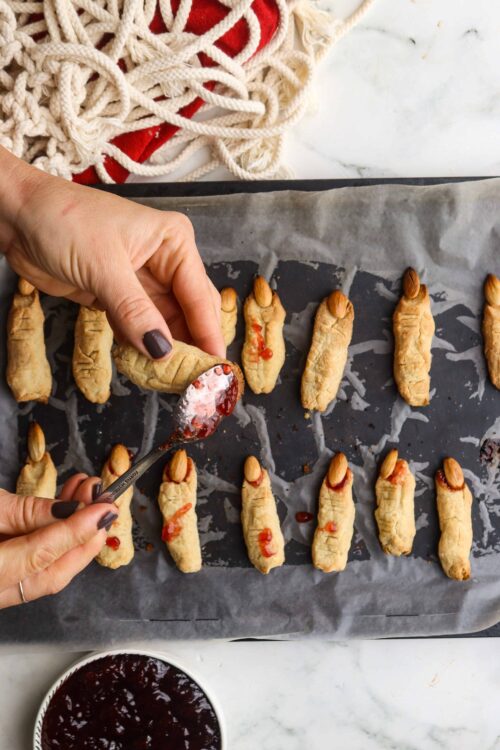 Mini cherry hand pies on baking sheet with jam filling being spooned into crusts.