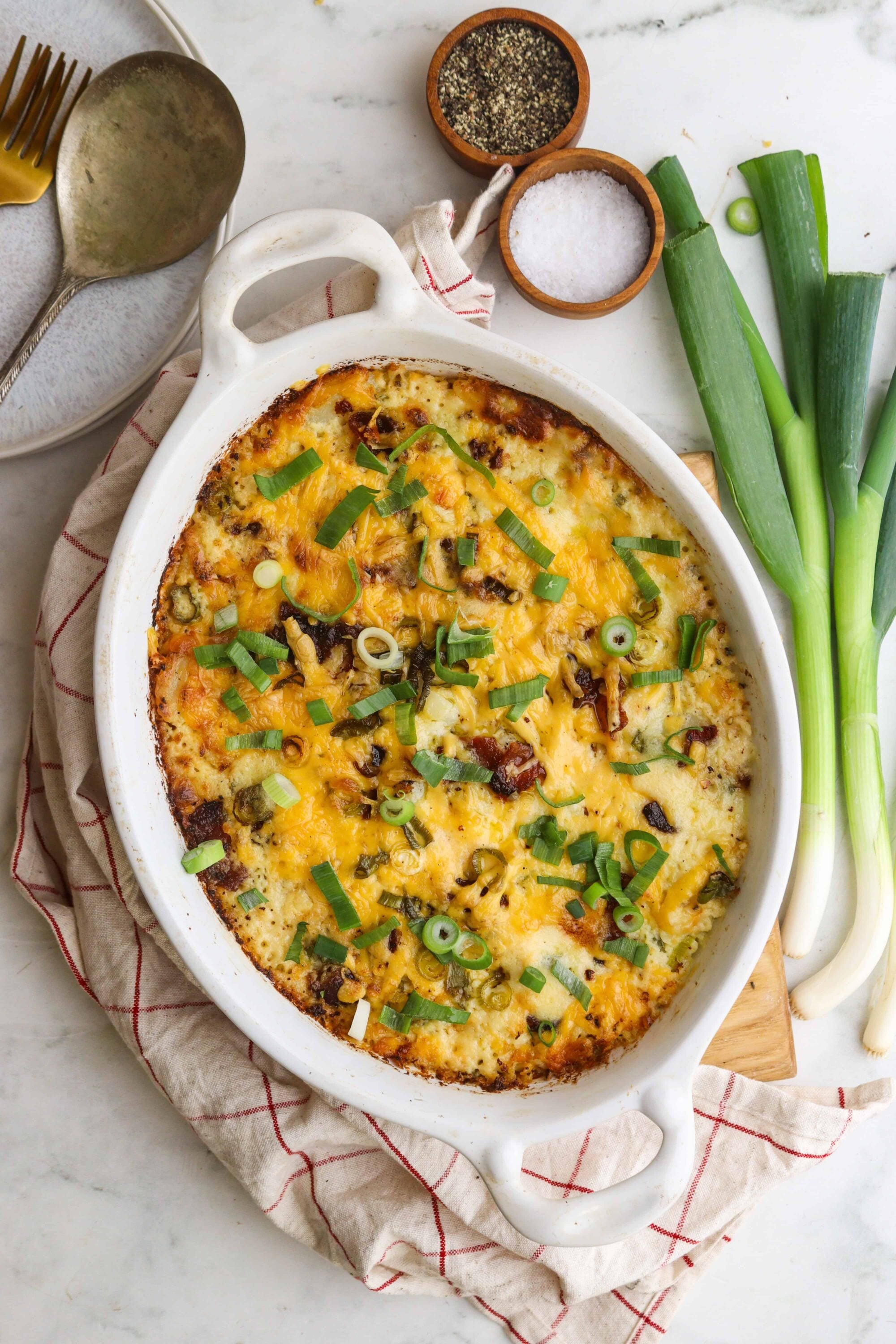 Creamy baked casserole with cheese, bacon, green onions, and herbs in a white baking dish.