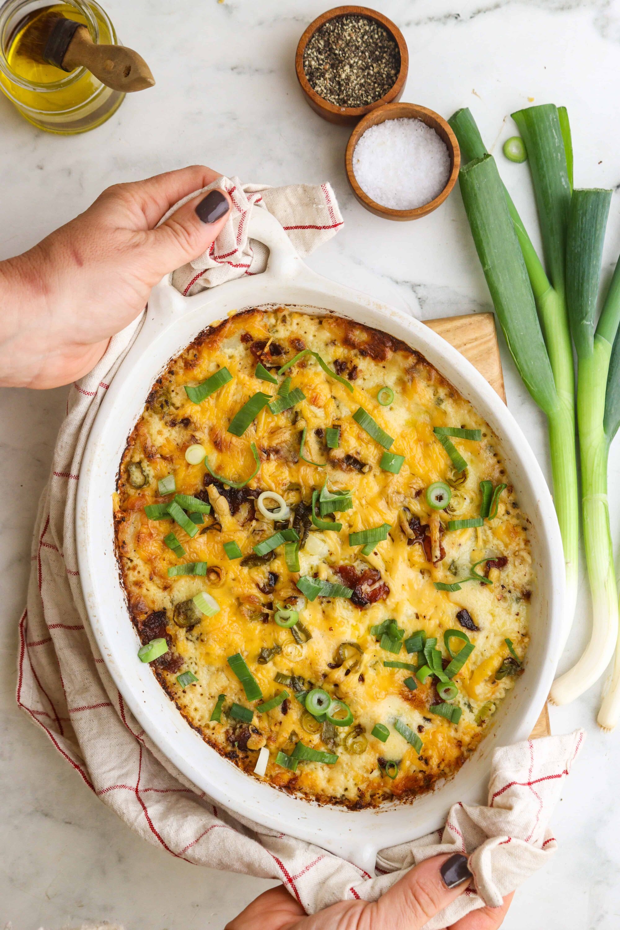 Creamy baked cheesy casserole with green onions and bacon garnish.