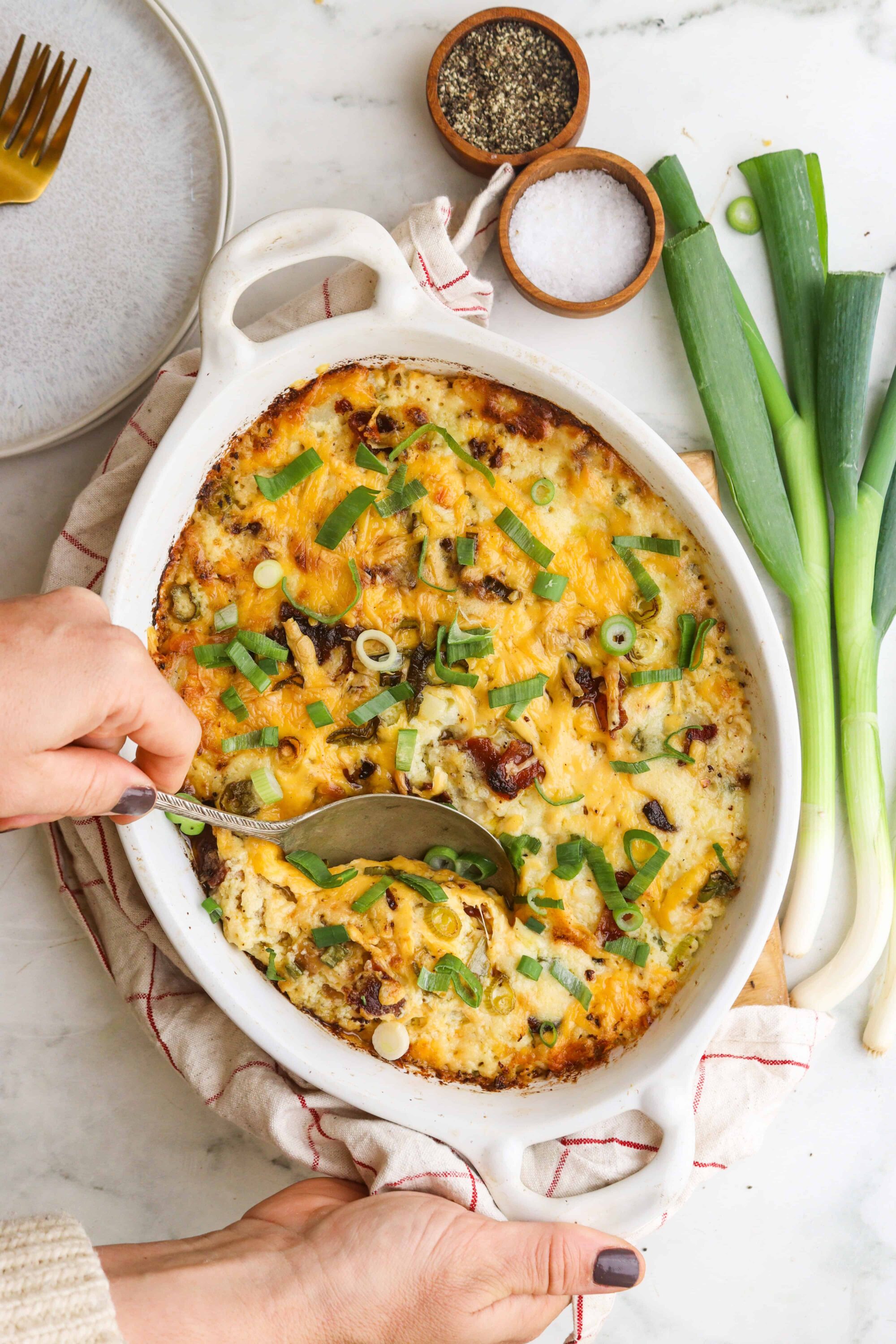 Cheesy baked casserole with green onions in a white baking dish.