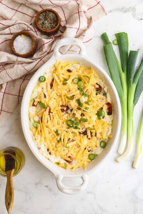Creamy baked potato casserole with cheddar cheese, green onions, and bacon in a white baking dish.