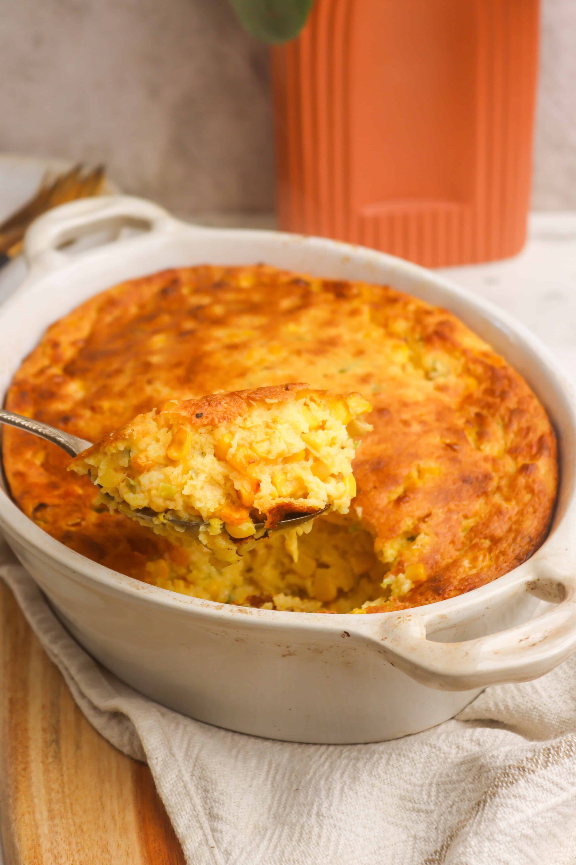Creamy corn casserole baked in a white dish topped with melted, golden cheese.