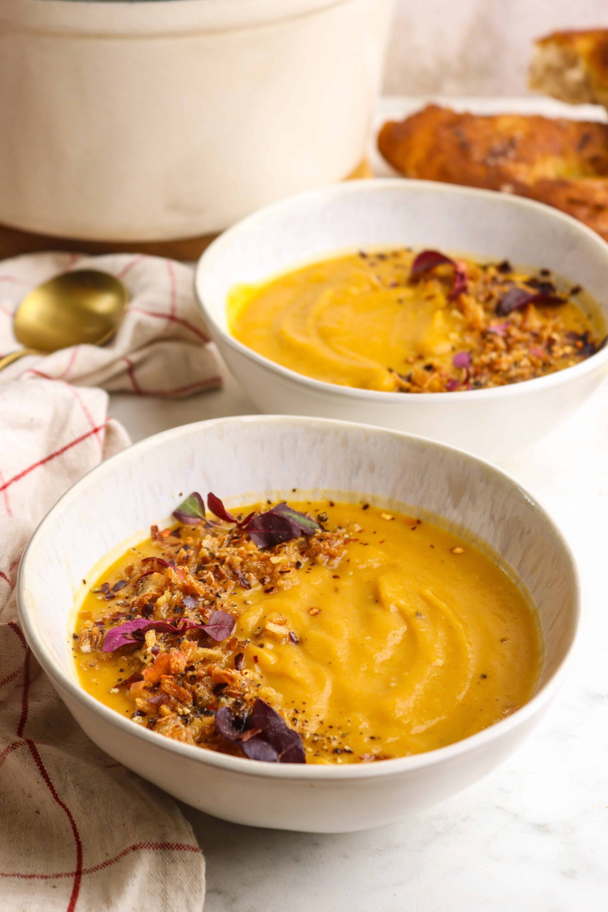Savory butternut squash soup with crispy bacon and garnishes in white bowls.