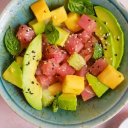 Fresh tuna poke bowl with avocado, pineapple, cucumber, and sesame seeds, served in a blue ceramic bowl.