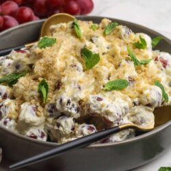 Sweet grape salad with creamy dressing and crushed cookies, garnished with fresh mint leaves. Perfect for summer or holidays.