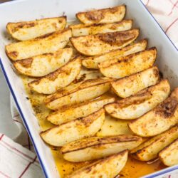 Golden baked potato wedges with crispy seasoning in a white baking dish.