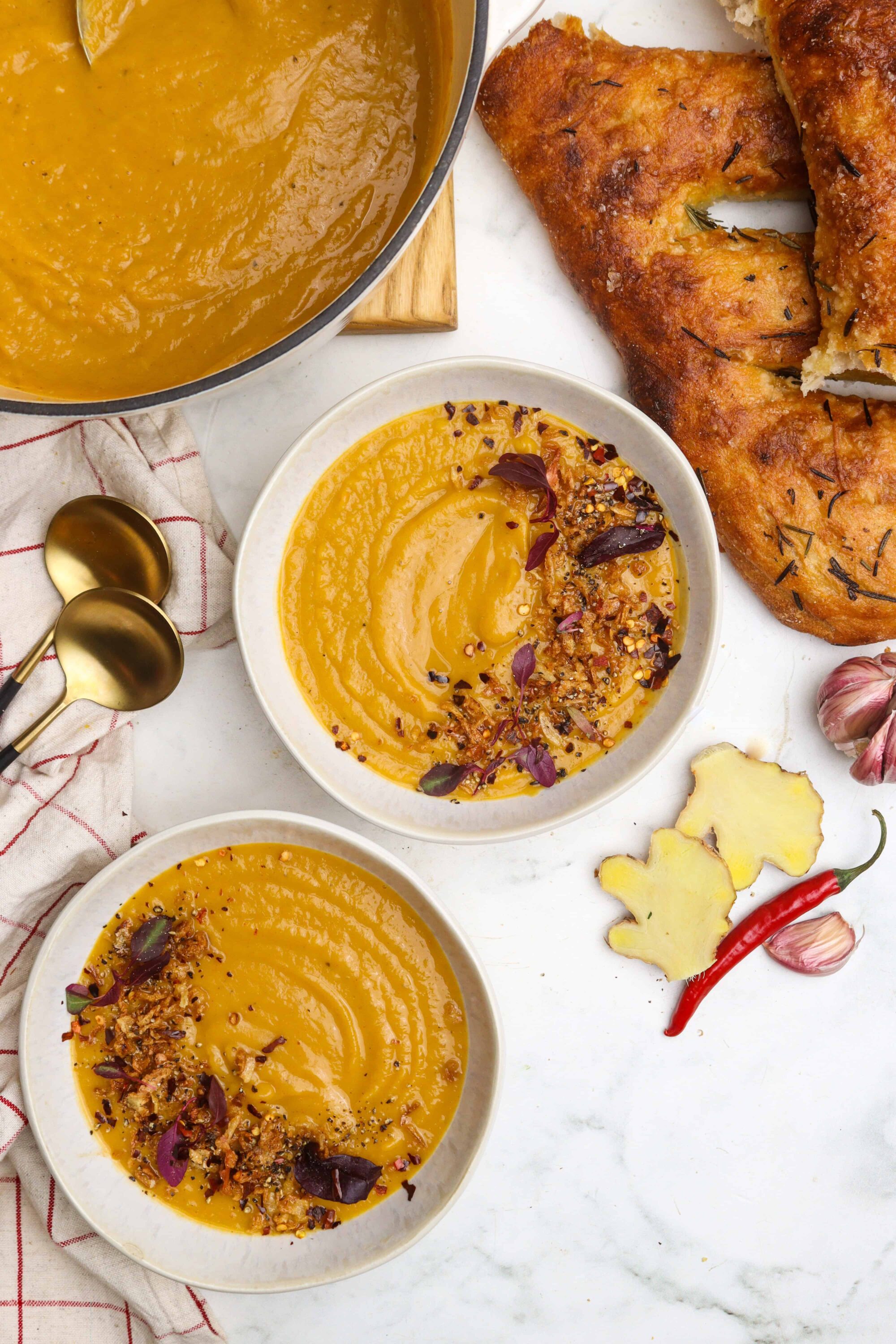 Creamy pumpkin soup with toasted spices and crunchy toppings on white bowls.