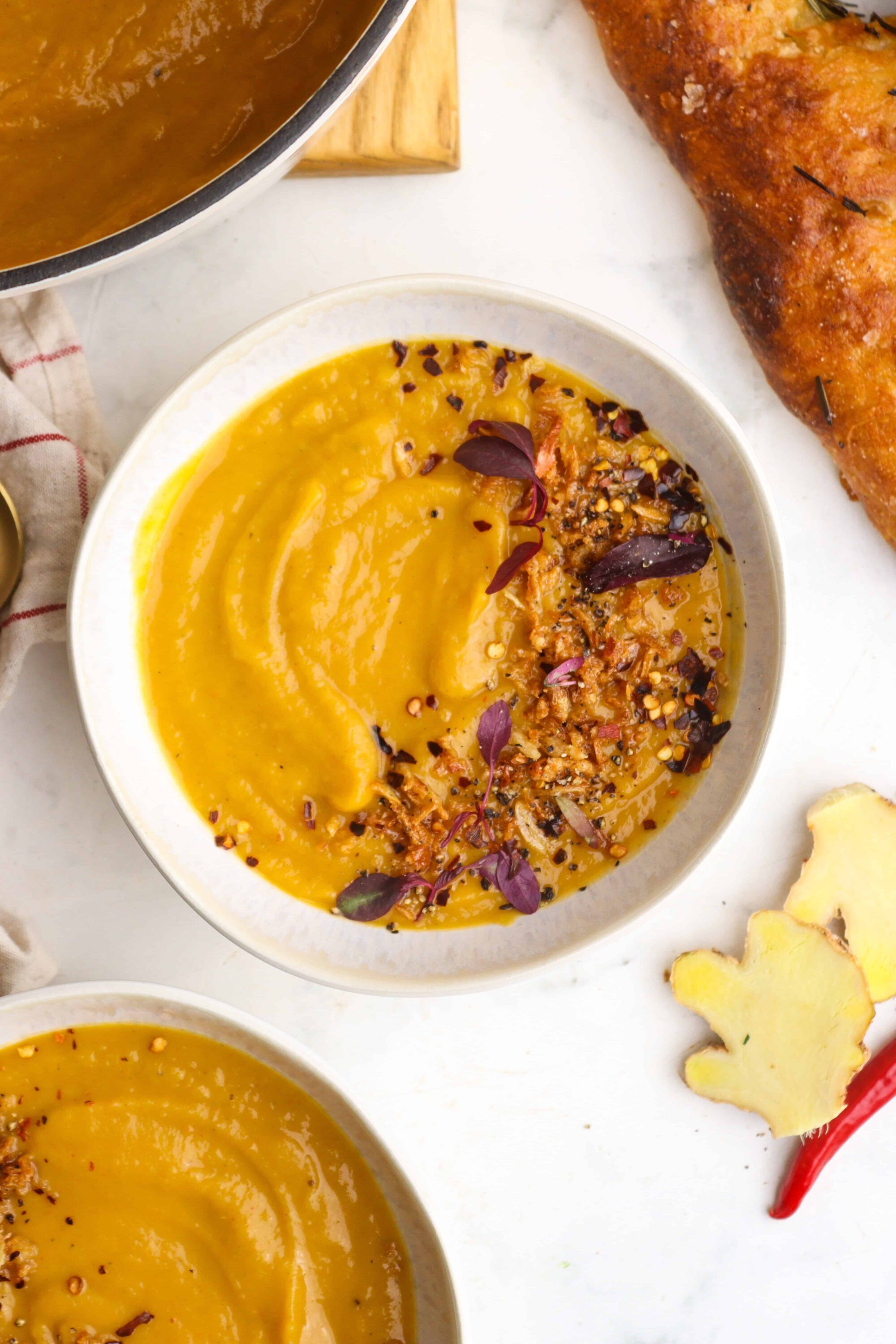 Creamy butternut squash soup garnished with chili flakes and microgreens, served in a white bowl.