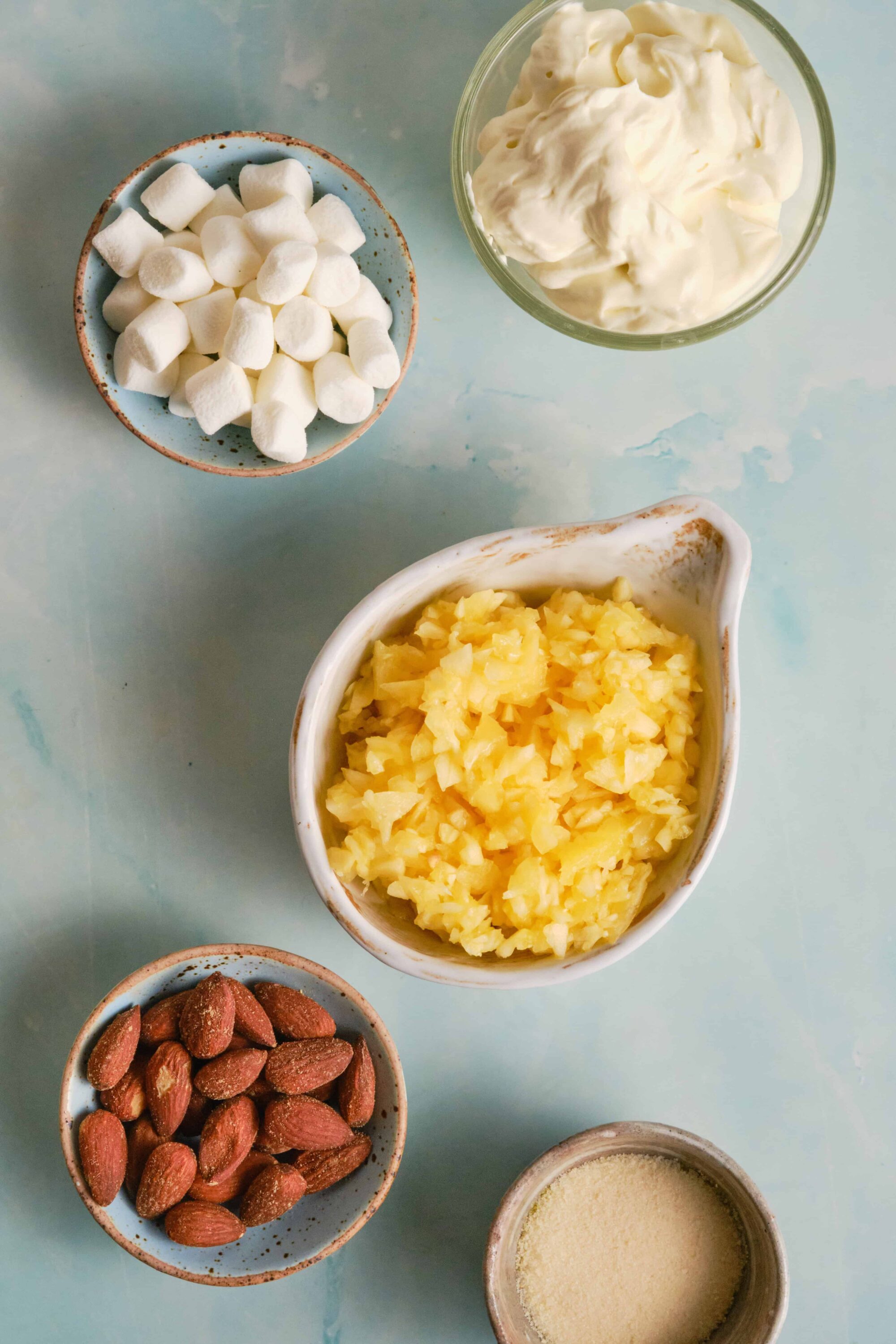 Cream cheese, shredded potatoes, almonds, marshmallows, and butter on a light blue background.