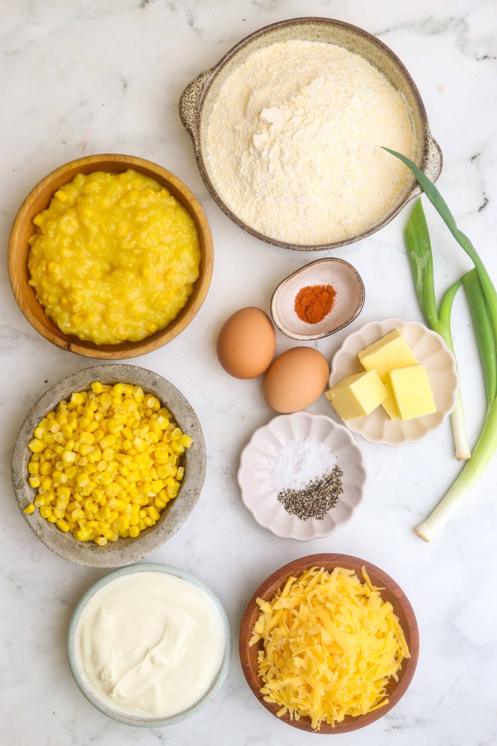Shredded cheese, corn, eggs, and baking ingredients for cheesy corn casserole.