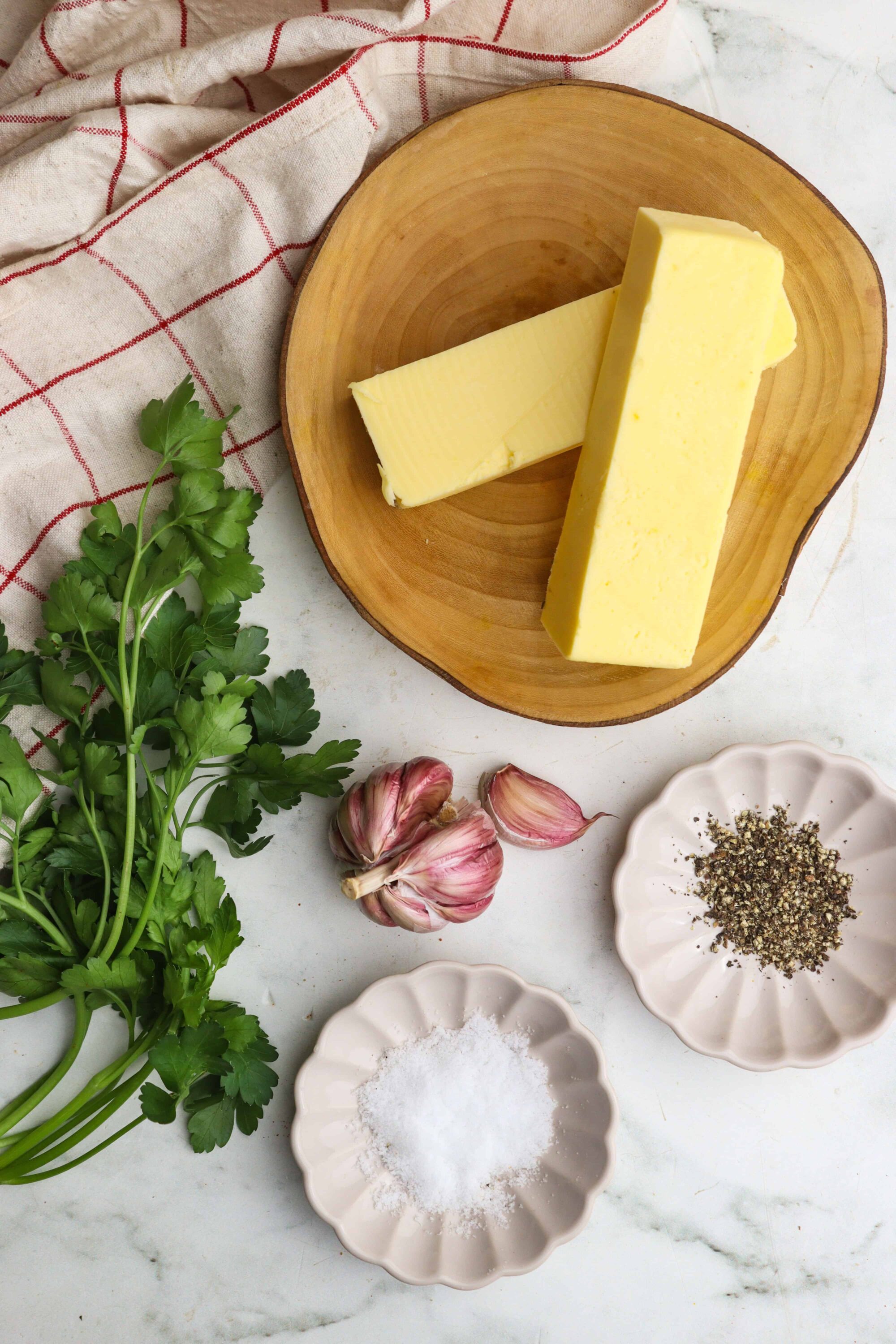 Creamy butter on a wooden plate with fresh herbs, garlic, salt, and pepper, perfect for cooking or baking.