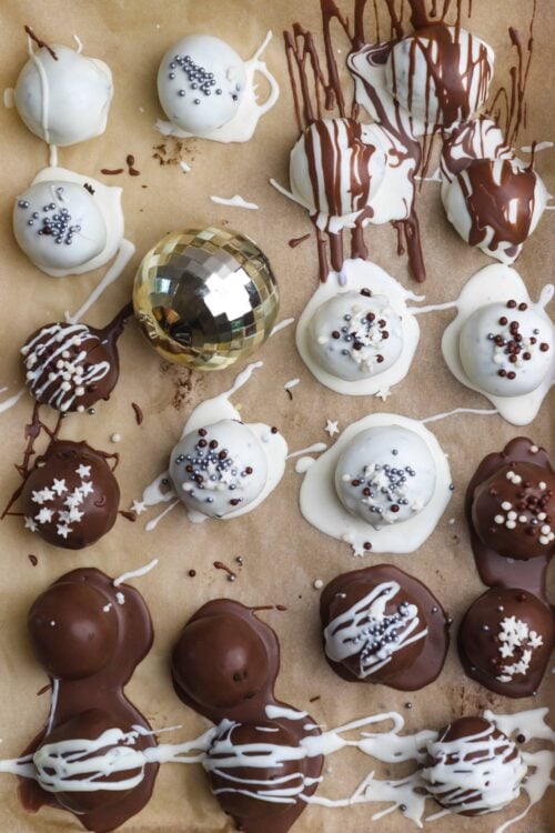 Decadent chocolate and vanilla Christmas cake balls with sprinkles and drizzle on parchment paper, festive holiday treat.