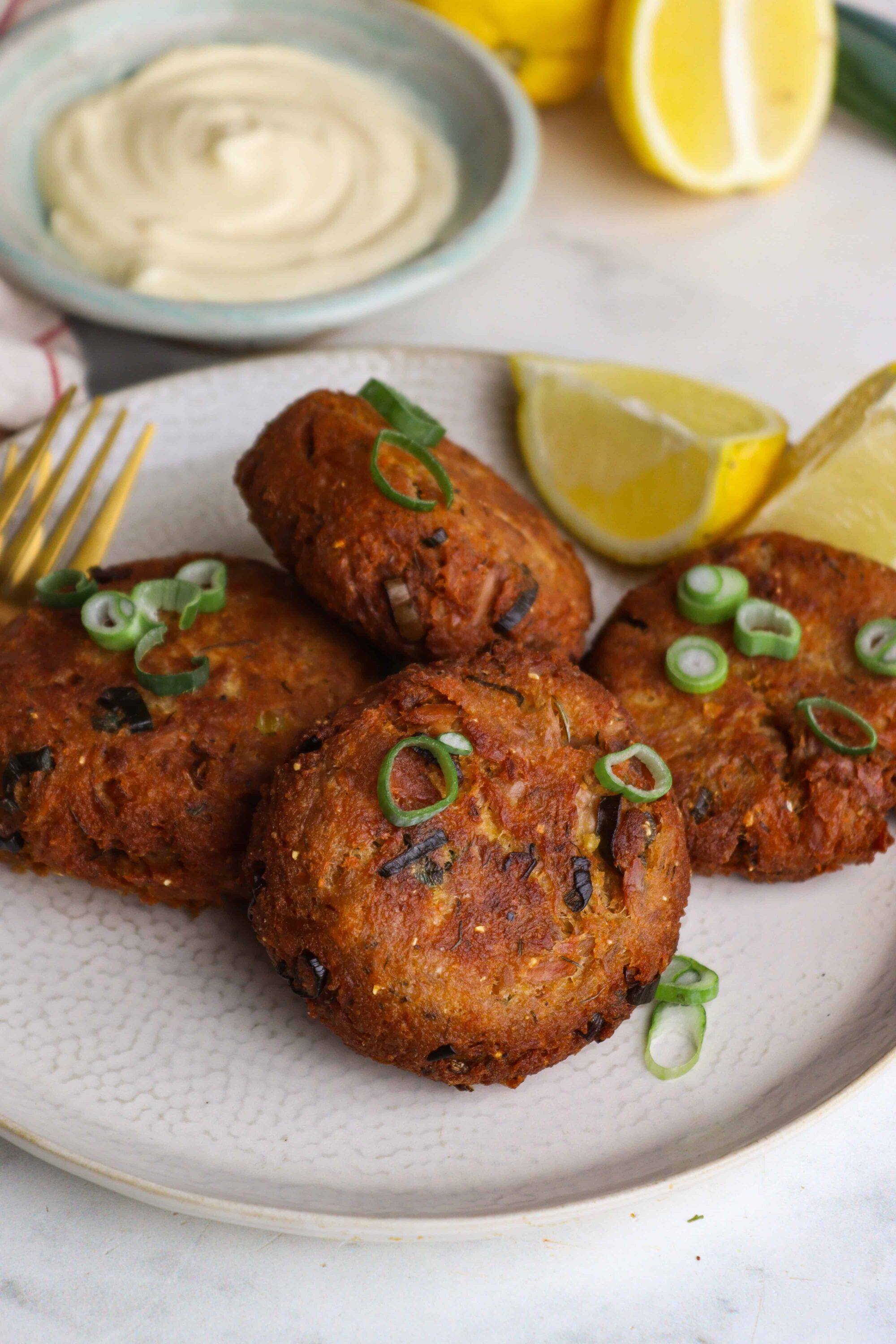 Golden-brown crab cakes with green onions and lemon wedges on white plate.